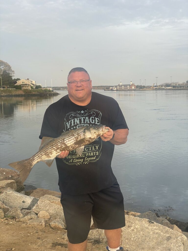 An excited fisherman holding a striped bass (aka striper) caught on a shaddy daddy lure at the Cape Cod Canal